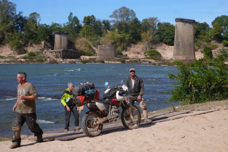 Explore Indochina riders next to a ruined bridge