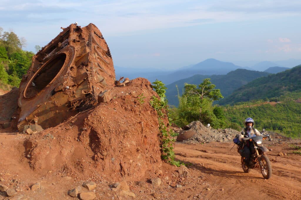 An Explore Indochina rider passes destroyed tank while on a Ho Chi Minh Trail motorbike tour