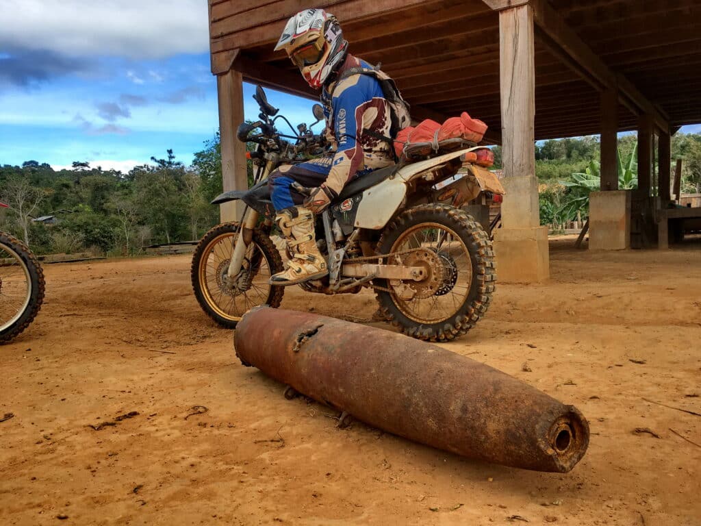 An Explore Indochina rider checking out a bomb casing near Ta Oi Laos while riding the Ho Chi Minh Trail