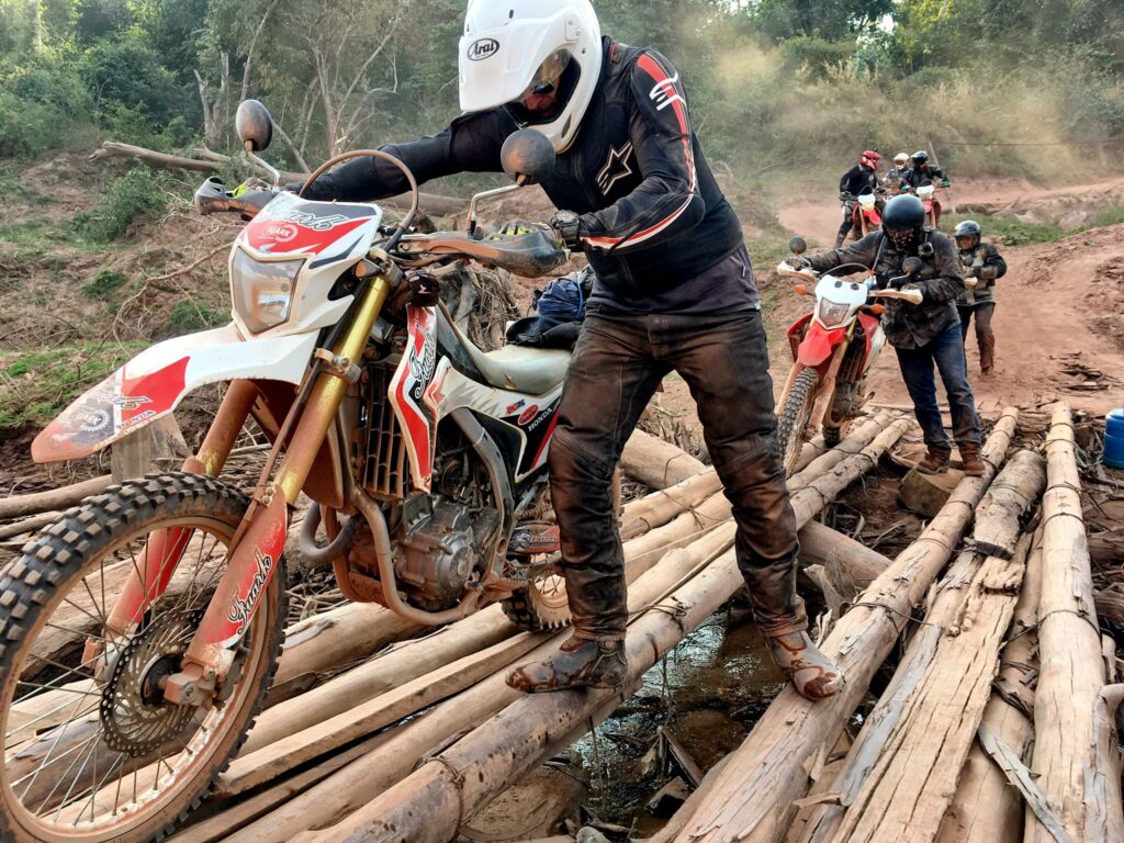 Explore Indochina riders crossing a bamboo bridge in Laos while on a Ho Chi Minh Trail motorbike tour