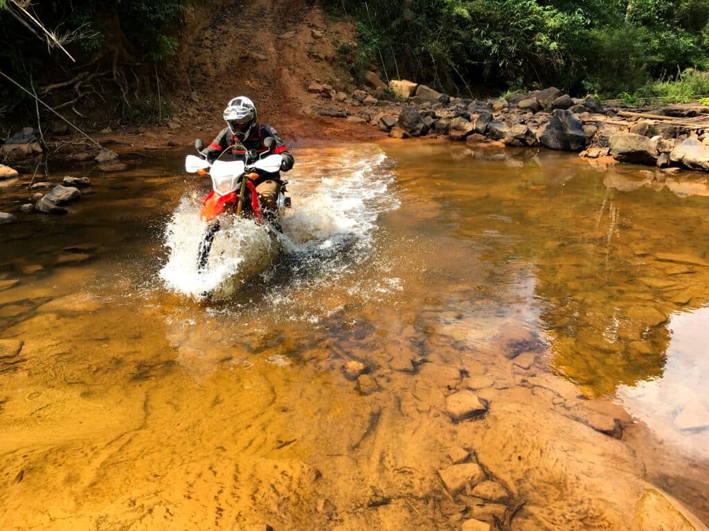Riding across a jungle stream on the Ho Chi Minh Trail near Nong in Laos while on a motorcycle tour
